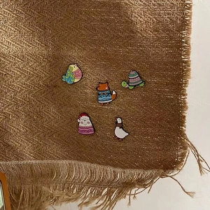 Detail of cute animal enamel pins including a goose, fox, and turtle on woven fabric