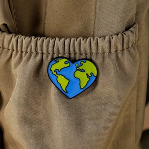Detail of heart-shaped earth enamel pin on a brown fabric bag with map design