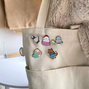 Cartoon animal enamel pins set featuring goose and fox on beige canvas bag