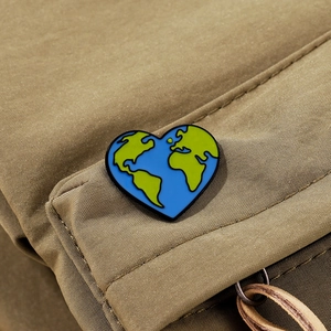 Macro shot of heart-shaped earth enamel pin on khaki canvas background showing texture