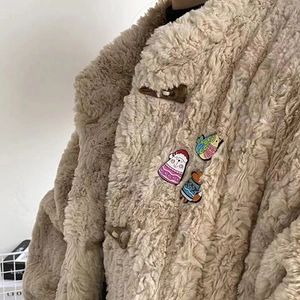 Close-up of cartoon animal enamel pins on a fleece jacket featuring cat and fox motifs