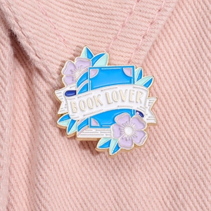 Macro shot of a Book Lover enamel pin with floral details on pink denim fabric
