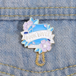 Détail d'un pin's en émail Book Lover avec fleurs sur une poche de veste en denim