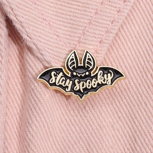 Détail du pin's chauve-souris Stay Spooky émaillé noir et doré sur tissu rose clair
