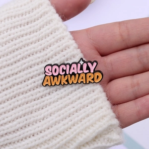 Socially Awkward enamel pin with pink and orange letters on white knitted sweater