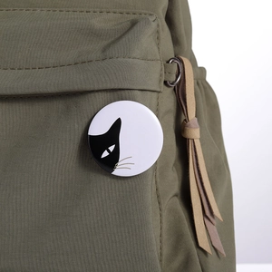 Close-up of a round minimalist black and white cat badge pinned on a green canvas backpack