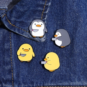 Gros plan de pins en émail pingouin et canard rigolos avec couteaux sur veste en jean