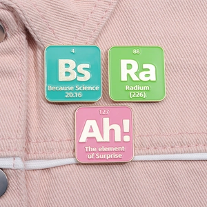 Detail of three colorful enamel chemistry element pins on pink denim fabric