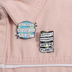 Detail van emaille pins op denim met de slogan Destroy the Patriarchy Not the Planet