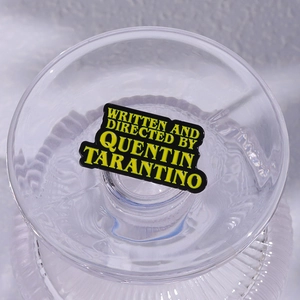 Gros plan d'un pin's en émail noir avec texte jaune Written and Directed by Quentin Tarantino