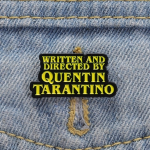 Pin's Quentin Tarantino en émail avec lettres jaunes sur métal noir sur denim