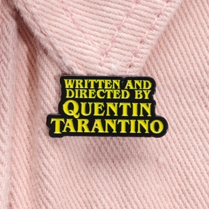 Détail macro d'une broche rectangulaire émaillée avec texte sur tissu rose