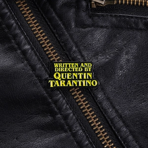 Détail d'un pin's émaillé Quentin Tarantino sur une veste en cuir noir avec fermeture éclair