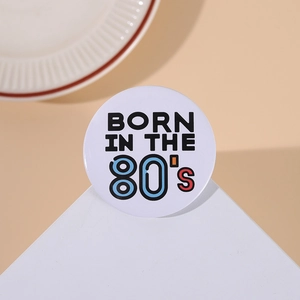 Close-up of a retro 'BORN IN THE 80's' round badge on a minimalist geometric stand