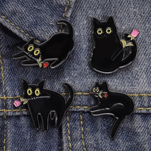 Détail de quatre épingles en émail chat noir avec roses sur tissu en jean bleu
