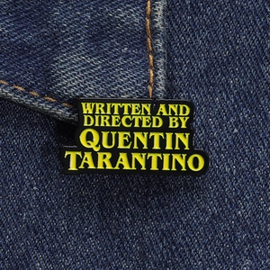 Détail macro d'un pin's en émail rectangulaire avec texte Quentin Tarantino sur denim