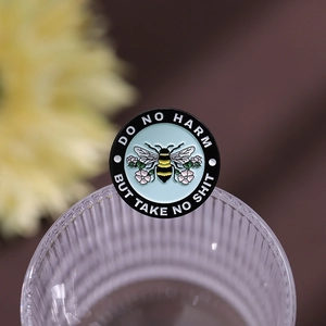 Macro view of a round enamel bee brooch featuring flowers and motivational text on glass