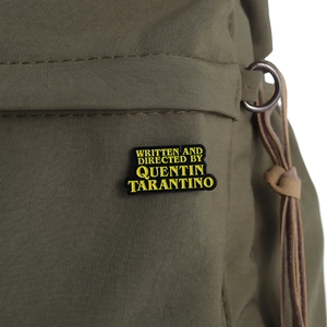 Détail d'un badge Quentin Tarantino épinglé sur un tissu en toile vert olive robuste