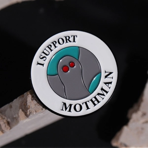 Macro detail of a round enamel Mothman badge with red eyes and I Support Mothman text