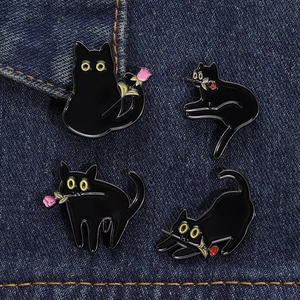 Détail de quatre pins en émail de chat noir avec des roses sur fond de denim bleu marine