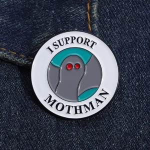 Macro detail of I SUPPORT MOTHMAN enamel pin on blue denim fabric background