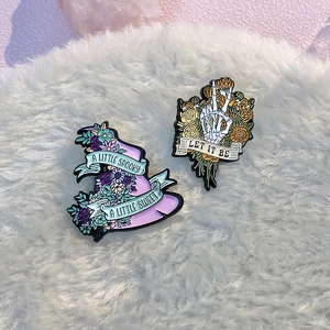 Detailed view of spooky sweet witch hat and skeleton hand enamel pins on pink crystals