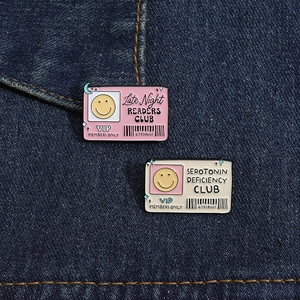 Detail of square enamel pins with club slogans on blue denim fabric texture