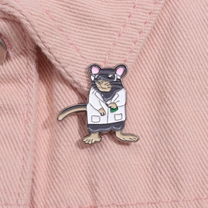 Macro shot of an enamel mouse scientist pin in a lab coat on pink fabric