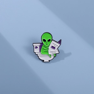Funny green alien ET pin sitting on a toilet reading a newspaper, creative enamel badge