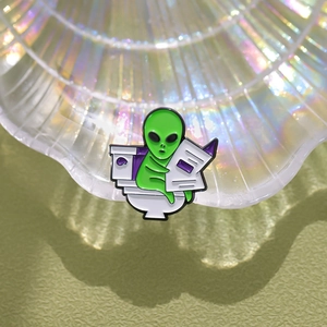 Detailed view of ET alien sitting on toilet reading book enamel pin on shell background