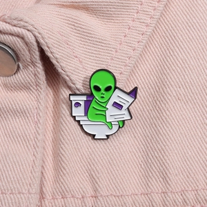 Detailed close-up of a funny green alien enamel pin on a pink denim jacket