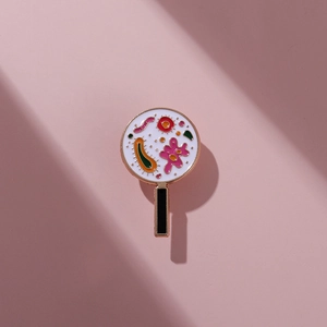 Dettaglio macro della spilla smaltata con motivi di batteri colorati e placcatura in oro rosa