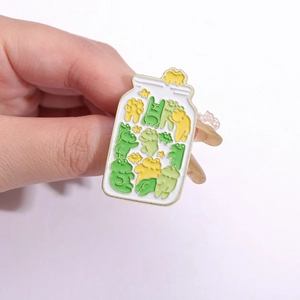 Close-up of a creative metal badge featuring cute cartoon frogs inside a white jar