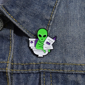 Funny alien sitting on a toilet reading a newspaper enamel pin on a denim jacket