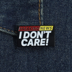 Vista macro della spilla smaltata BREAKING NEWS I DON'T CARE su sfondo denim blu