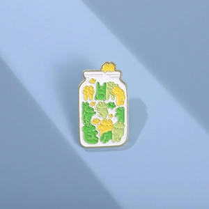 Detailed view of the frog jar enamel pin with green cartoon frogs and polished metal edges