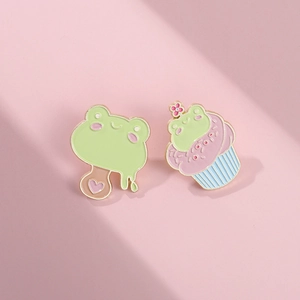 Primer plano de lindos pines esmaltados de rana en forma de helado y cupcake rosa