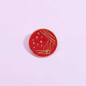 Creative red Petri dish enamel pin with golden bacterial colony patterns on purple background