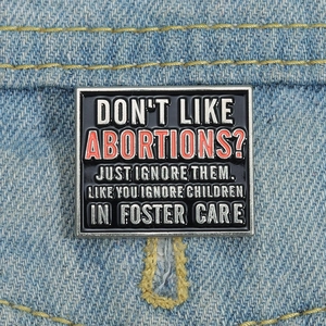 Spilla smaltata geometrica vintage con slogan sociale su denim, finitura nera e argento