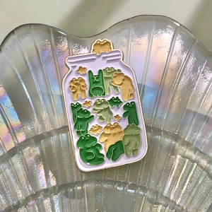 Detail of creative jar-shaped enamel pin with colorful cartoon frogs and golden edges