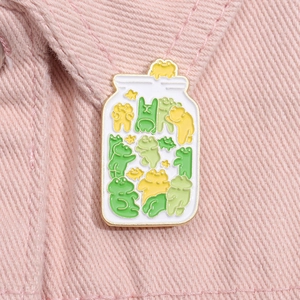 Macro shot of an enamel jar pin filled with cute colorful cartoon frogs on denim fabric