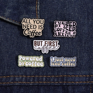 Detailansicht von fünf Emaille-Anstecknadeln zum Thema Kaffee auf blauem Denim-Stoff
