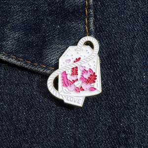 Dettaglio della spilla smaltata a forma di bustina di tè con fiori e scritta LOVE su denim