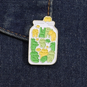 Close-up of a creative frog glass jar enamel pin on blue denim fabric background
