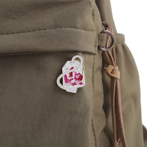 Dettaglio di una spilla smaltata creativa a forma di bustina di tè Love su borsa in tela