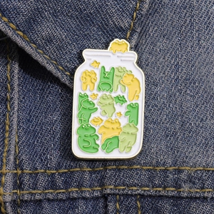 Detailed close-up of a cute enamel frog jar pin displayed on dark blue denim fabric