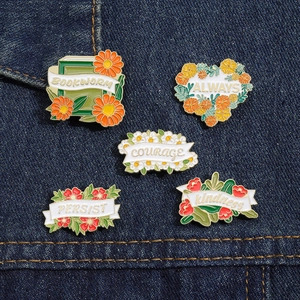 Close-up of five floral enamel pins with motivational words on blue denim fabric