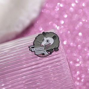 Detail of funny opossum enamel pin on a glass rim with Awesome Possum text detail