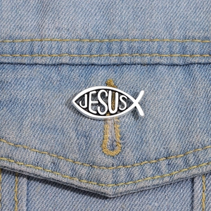 Close-up of silver metal Ichthys fish brooch with Jesus text on blue denim jacket pocket
