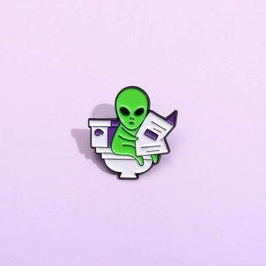 Funny alien enamel pin sitting on toilet reading newspaper made of metal alloy